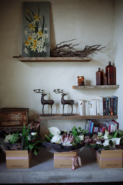 Boxed bouquets of white anthurium, king protea and roses sit beneath shelves of books and deer figurines.