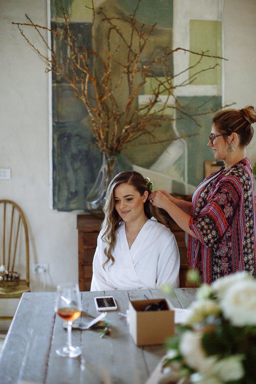 Seated at a timber table, Elysha smiles as a stylist pins flowers into her hair.