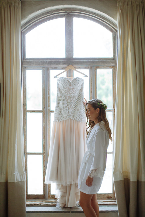 Elysha in her robe reaches up to the beaded lace gown hanging in the arched window.
