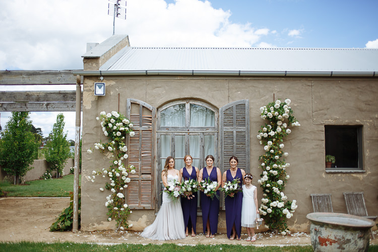 Elysha, three bridesmaids in navy and the flower girl line up before the rose framed shuttered window.