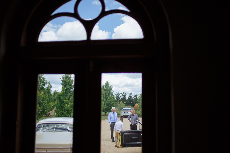 Through a fanlight door, three men load a golf bag beside a cream vintage car.