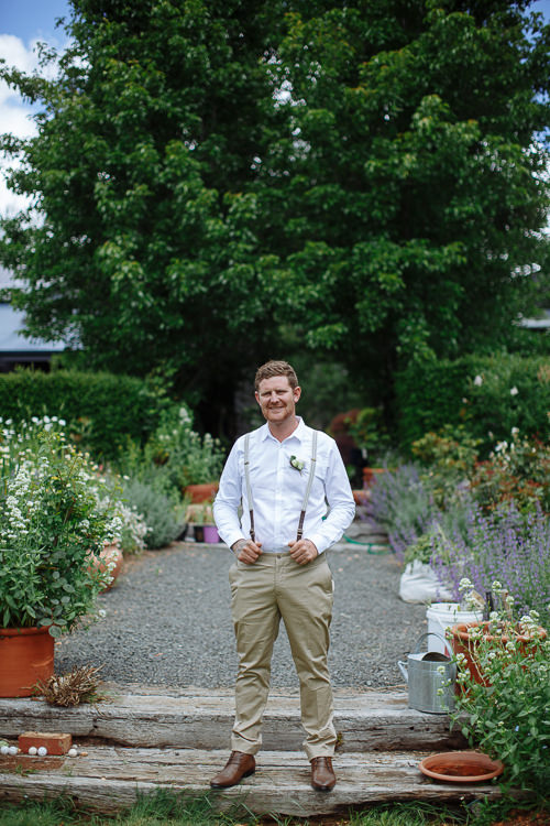 In a white shirt, tan chinos and brown braces, Mitch smiles on a sleeper step among pots.