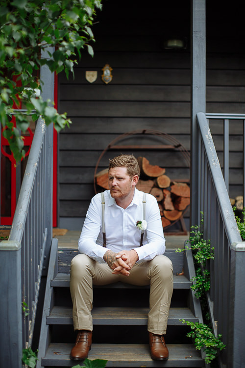 Seated on grey timber steps before a black weatherboard wall, Mitch looks off to the left.