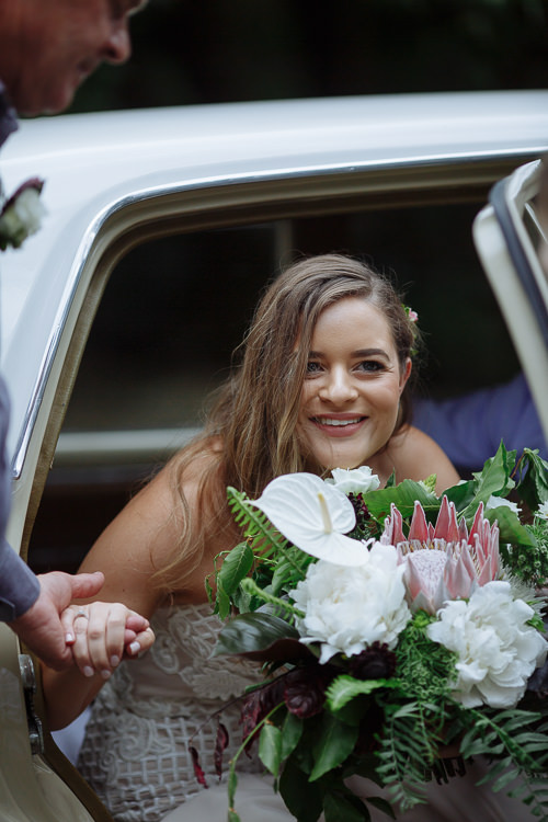 Elysha smiles from the back seat of the cream car as a hand helps her out.