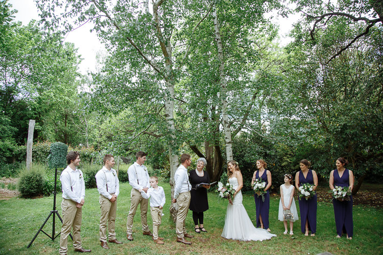 Wide view of the garden ceremony at The Cosmopolitan Hotel beneath silver birches, bridesmaids in navy.