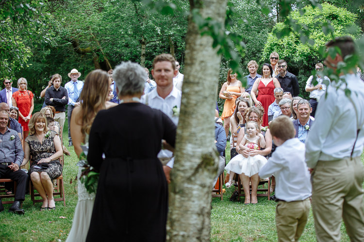 Past a birch trunk, the celebrant and Elysha face Mitch and the guests on the lawn.