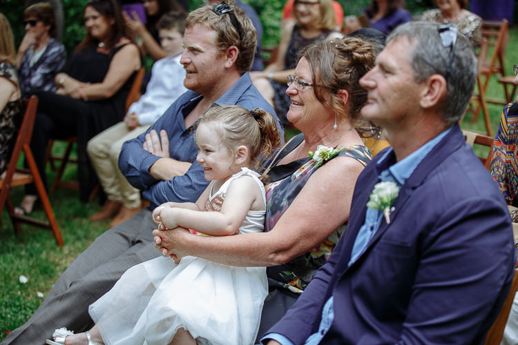 A small girl in white sits on a guest's lap beside a woman with a corsage.