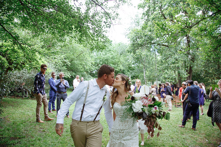 The couple kiss as they walk back through the garden hand in hand past guests with phones.