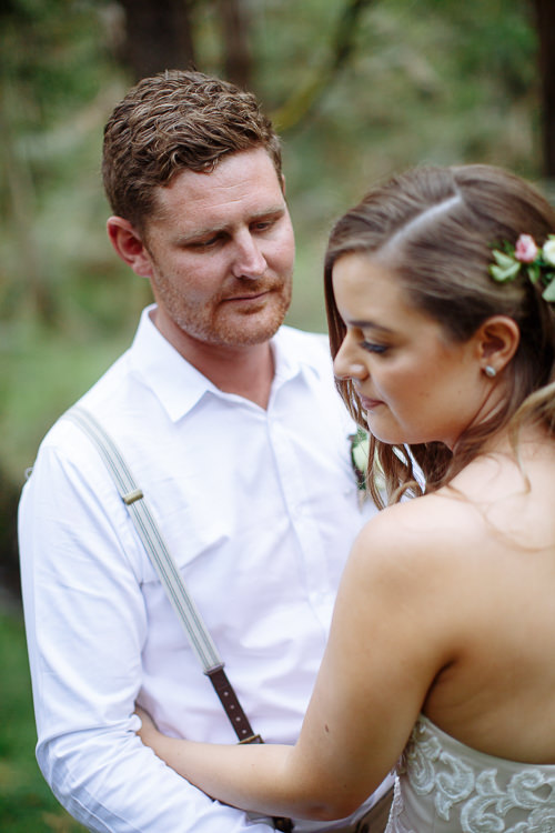 Mitch looks down at Elysha, who looks down with roses pinned in her hair.