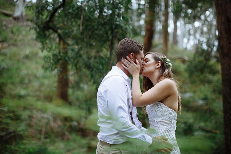 Among ferns and gum trunks, Elysha holds Mitch's face and kisses him.