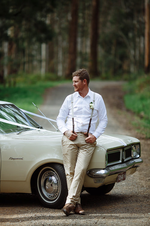 Leaning on the bonnet of the ribboned cream sedan on a forest road, Mitch holds his braces.