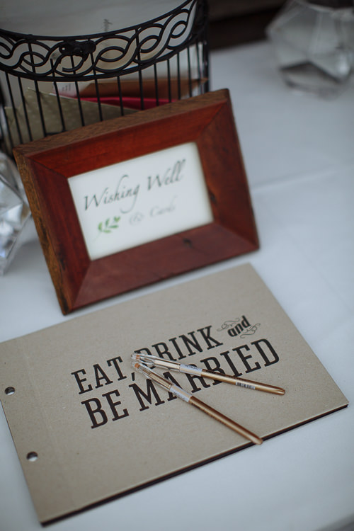 A framed wishing well sign beside a birdcage and a guest book lettered eat, drink and be married.