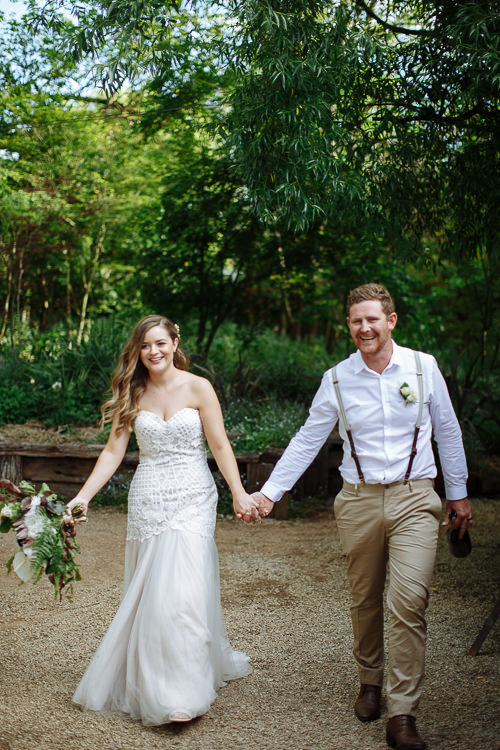 Elysha and Mitch walk hand in hand up the gravel path toward camera, both beaming.