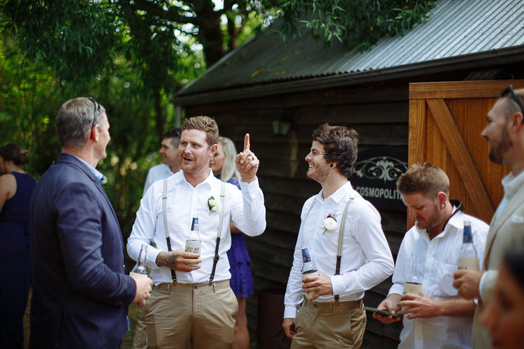 Mitch raises a finger mid story to a guest as a groomsman laughs beside the barn door.