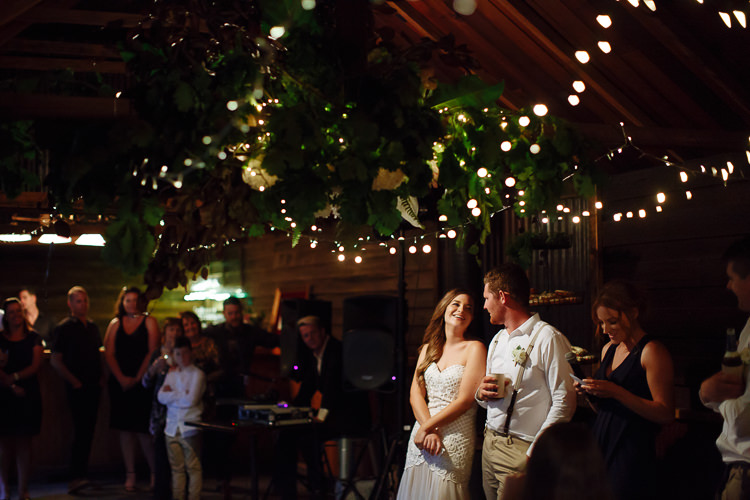 Under the hanging florals and festoon lights at The Cosmopolitan Hotel, Elysha looks up at Mitch.