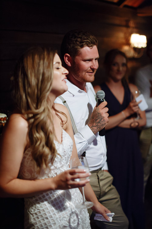 Speaking into the microphone with a tattooed arm, Mitch makes Elysha laugh beside him.