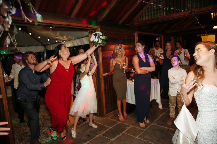 A woman in a red jumpsuit leaps for the tossed bouquet as a flower girl reaches up.