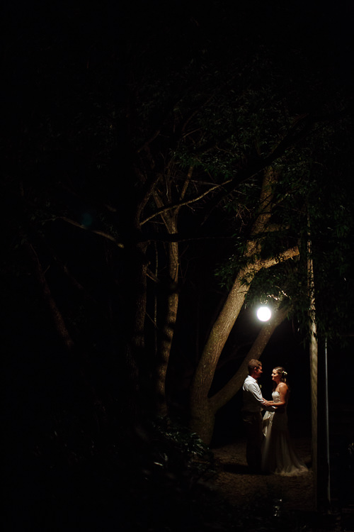 Tiny beneath dark trees at The Cosmopolitan Hotel, Elysha and Mitch stand lit by a single globe.