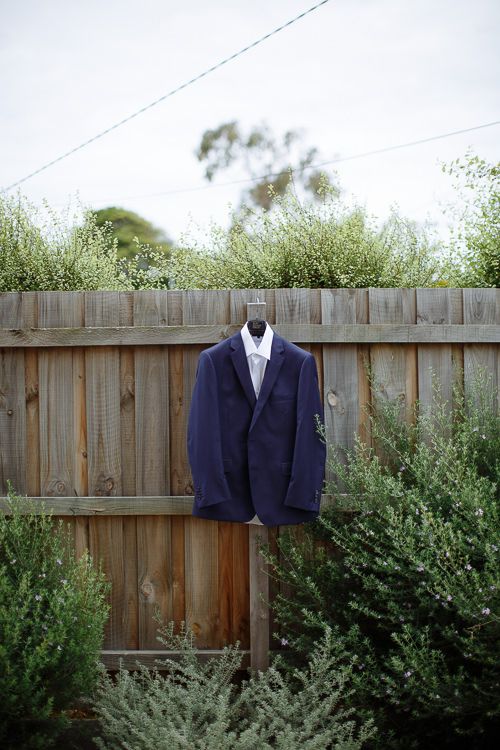 Groom's navy suit jacket hanging on a timber fence before the wedding