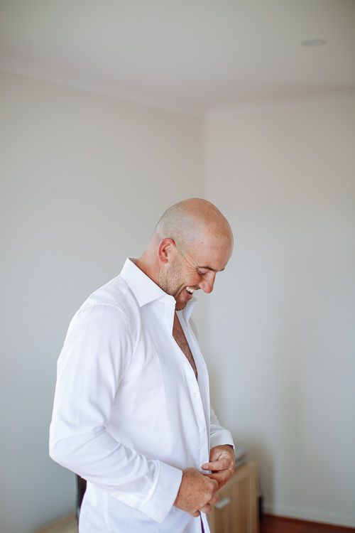 Groom buttoning his crisp white shirt during wedding preparations