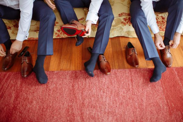 Groomsmen pulling on tan leather shoes and navy suit trousers