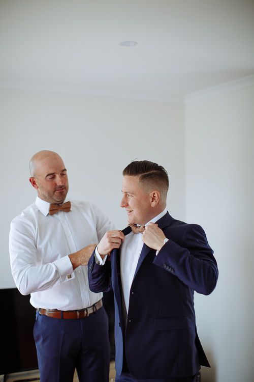 Groom straightening a groomsman's wooden bow tie