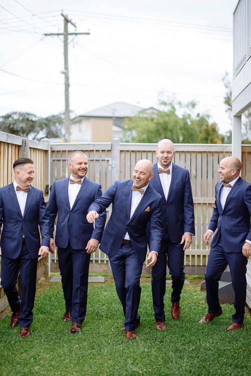 Groomsmen in navy suits and wooden bow ties laughing together outside