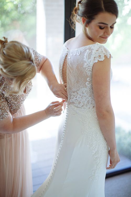 Mother buttoning the back of the bride's lace wedding gown