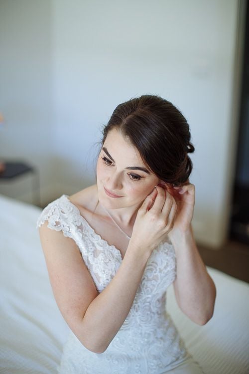 Bride fixing her earring in the window light
