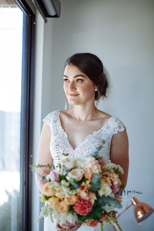 Bride at the window with her pastel bouquet in soft light