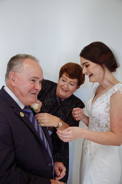 Grandparents pinning the boutonnière as the bride laughs