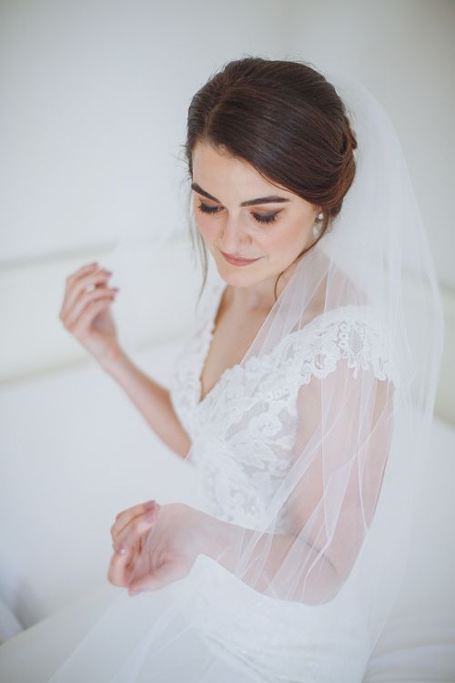 Bride touching her veil – romantic window-light portrait
