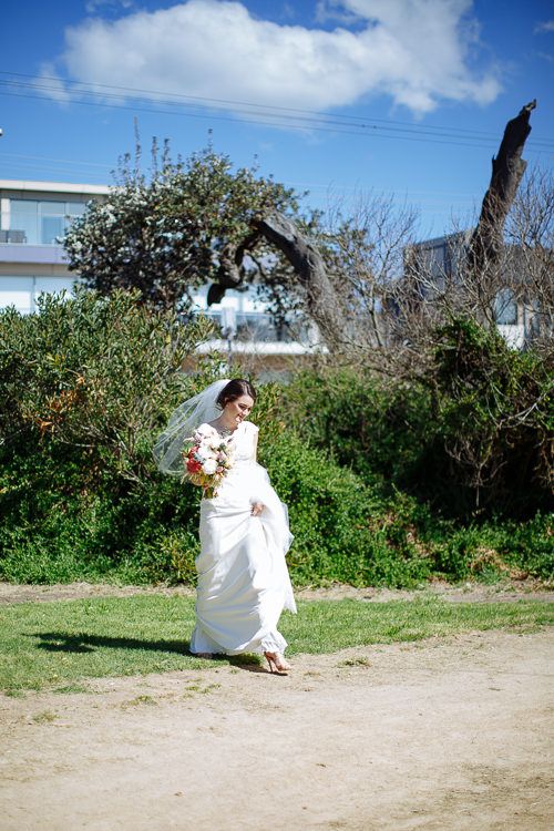 Bride carrying her gown across the grass toward the first look