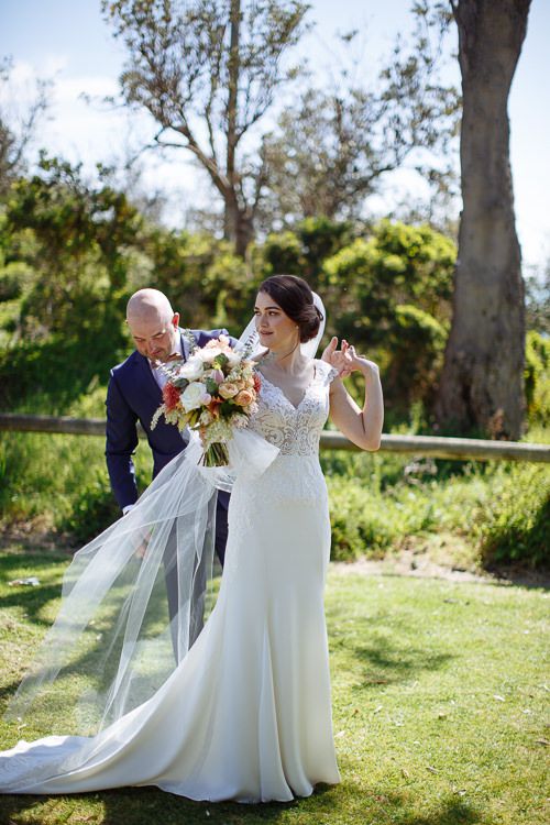 Groom helping the bride with her veil among the coastal trees