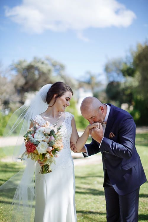 Groom kissing the bride's hand, peach bouquet in frame