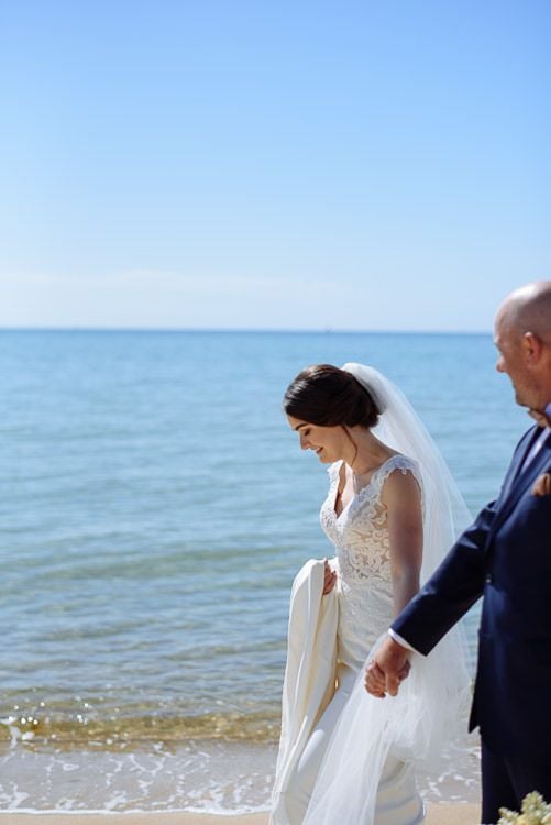 Bride smiling down as the couple walk the water's edge