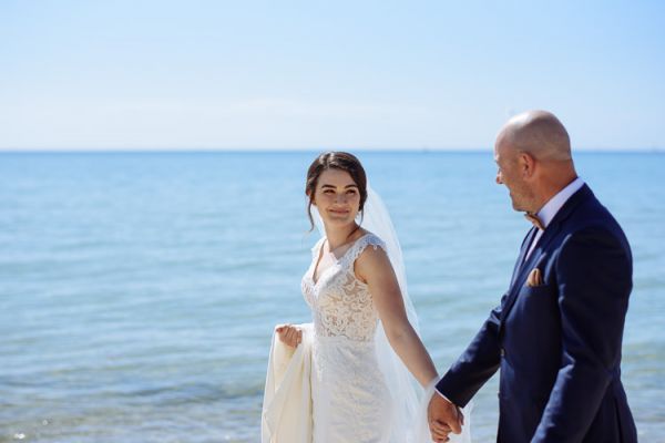 Bride and groom hand in hand against the blue of the bay