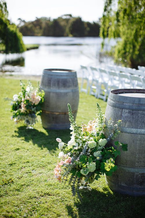 Wine barrels topped with florals beside the white ceremony chairs