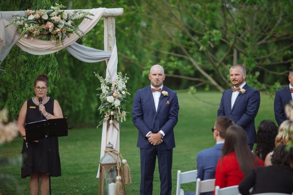 Groom and groomsmen waiting at the floral arch by the willows