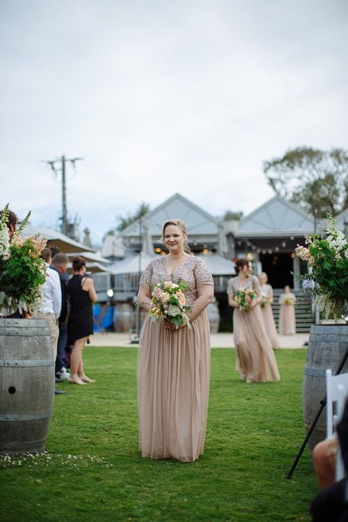 Bridesmaid in blush sequins walking down the garden aisle