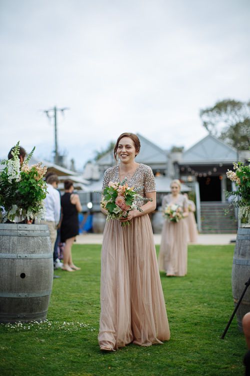 Bridesmaid smiling mid-processional with her peach bouquet