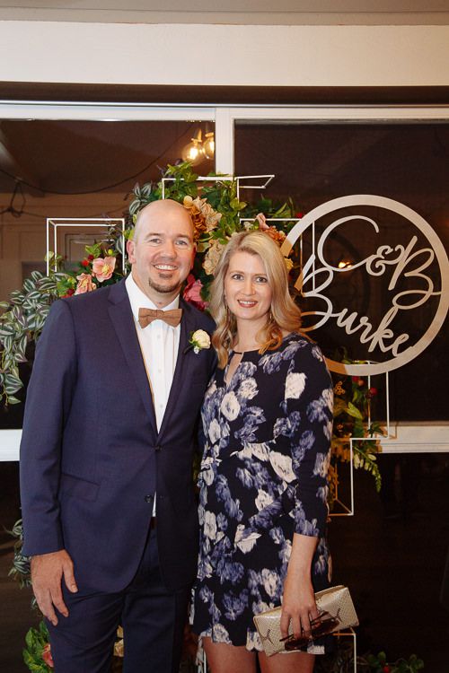 Couple posing by the floral wedding sign at the reception