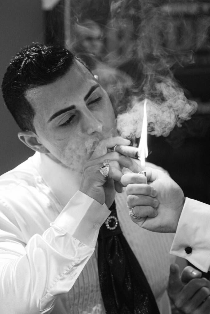 Black-and-white close-up of Michael lighting a cigar before the wedding