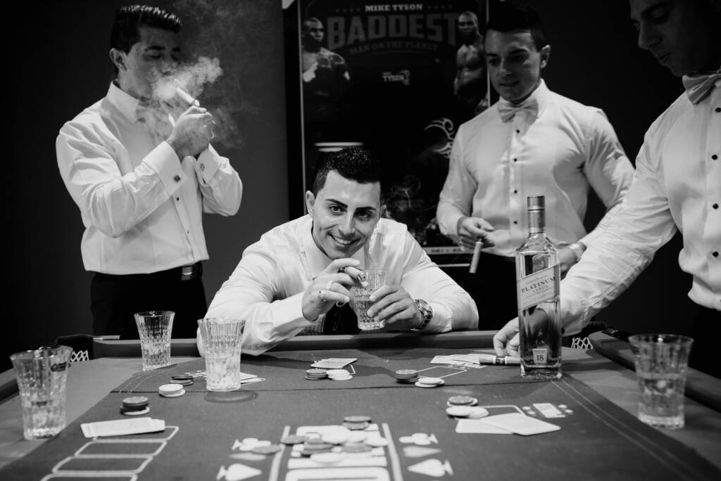 Michael smiles with a cigar and glass beside his groomsmen at the card table