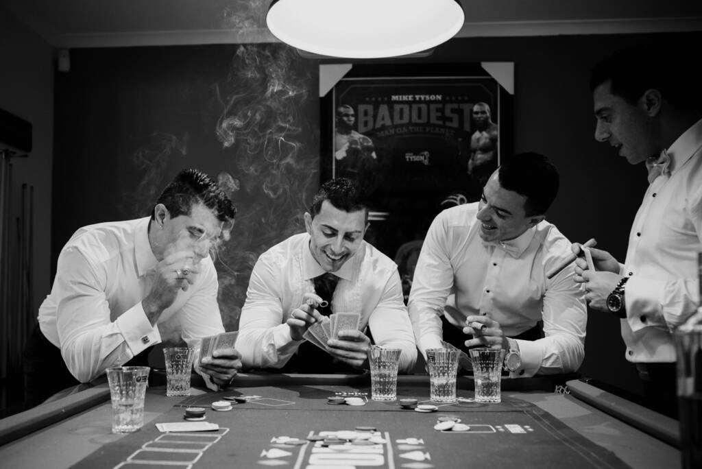 Michael looks at his playing cards while a groomsman exhales cigar smoke