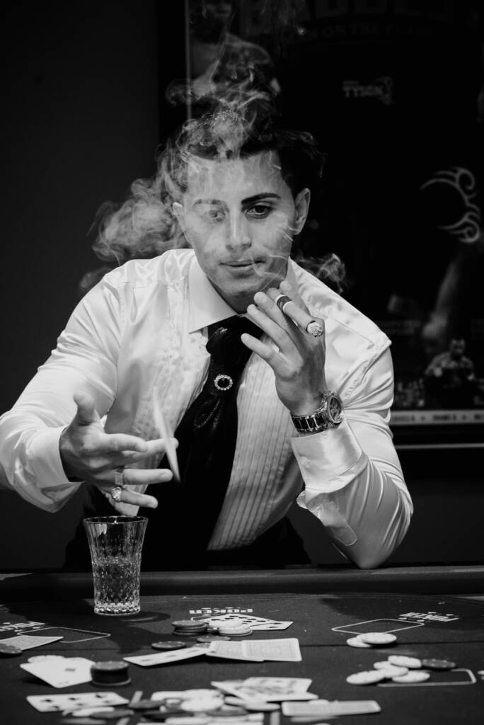 Black-and-white photo of Michael gesturing across the card table through cigar smoke