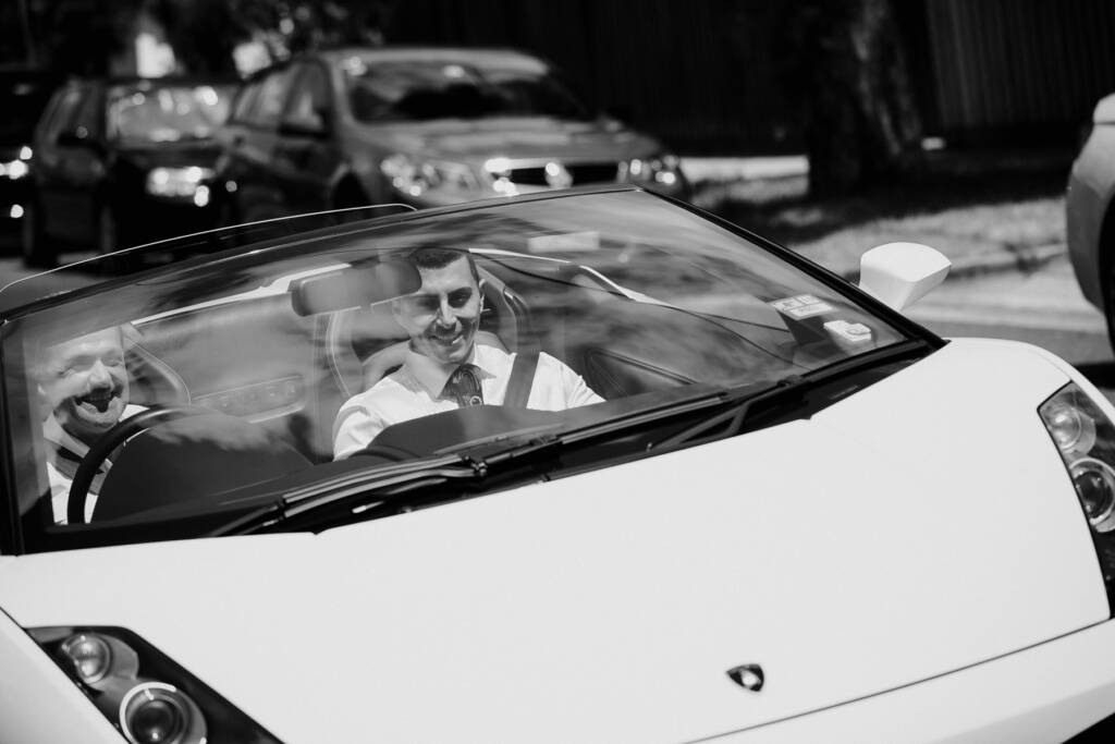 Michael rides in the passenger seat of a white convertible beside a smiling driver