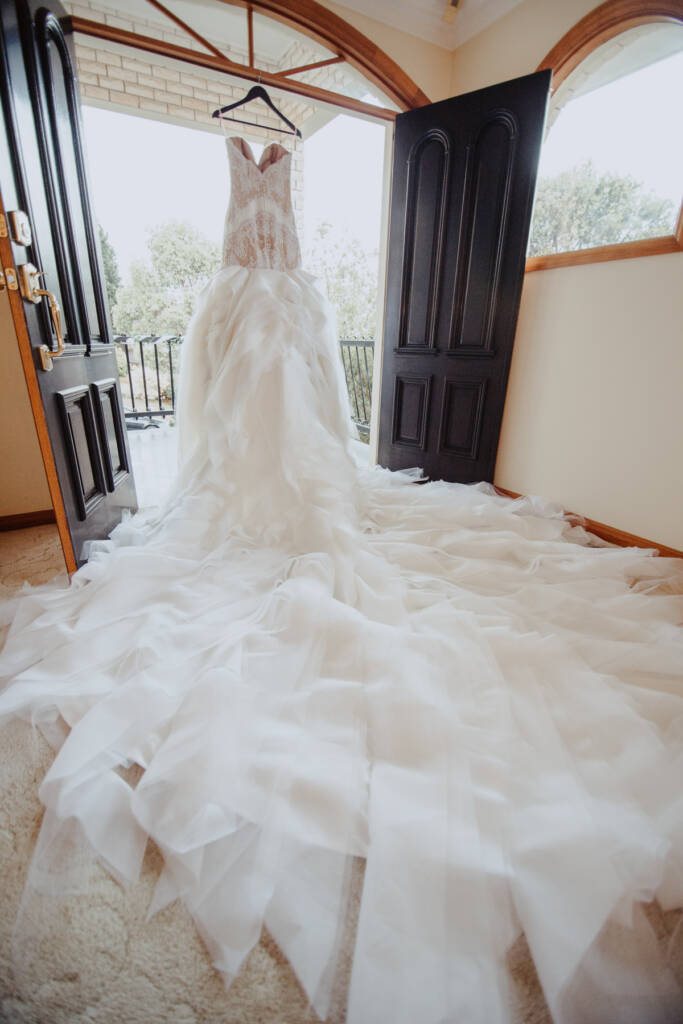 Danielle's lace wedding gown hangs in a doorway with its ruffled skirt spread below