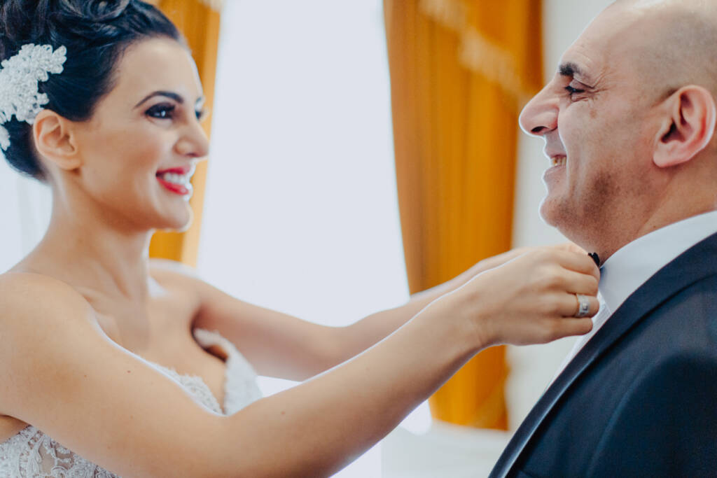 Danielle adjusts an older man's neckwear as they smile before the ceremony