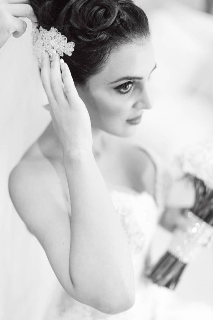 Black-and-white portrait of Danielle with a hand adjusting her bridal hairpiece